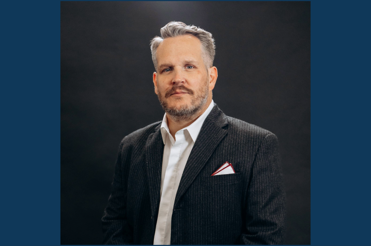 Portrait of man with neat beard in dark suit, white shirt.